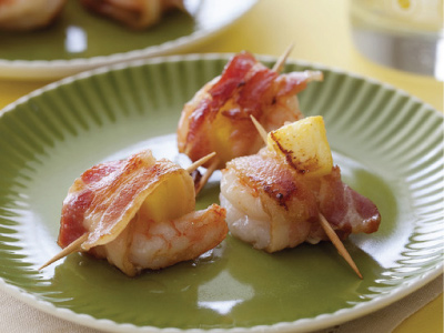 Three finished bacon raps in toothpicks on a green plate, sitting on a off yellow table.